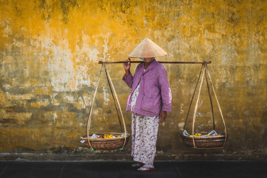 Vendeuse de rue devant un mur jaune à Hoi An, Vietnam